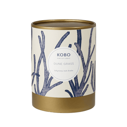Front view of Dune Grass Coastal Candle showcasing a gold-toned tin with blue grass artwork against a green background