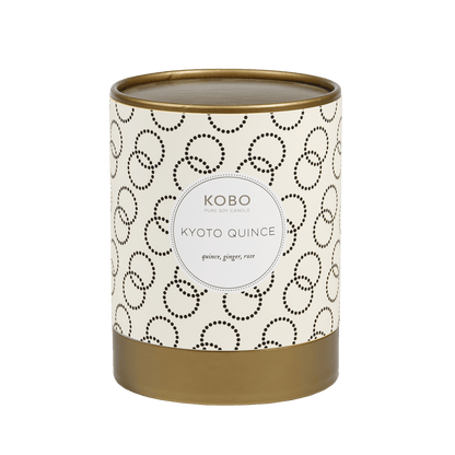 Front view of Kyoto Quince Coterie 11 oz candle with cream patterned vessel and gold base on green background