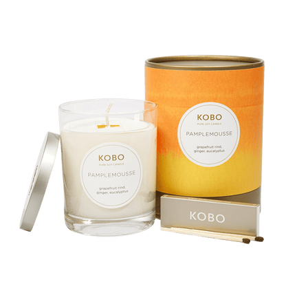 Front view of Pamplemousse Watercolor Candle showcasing grapefruit rind, ginger, and eucalyptus with orange packaging and matches